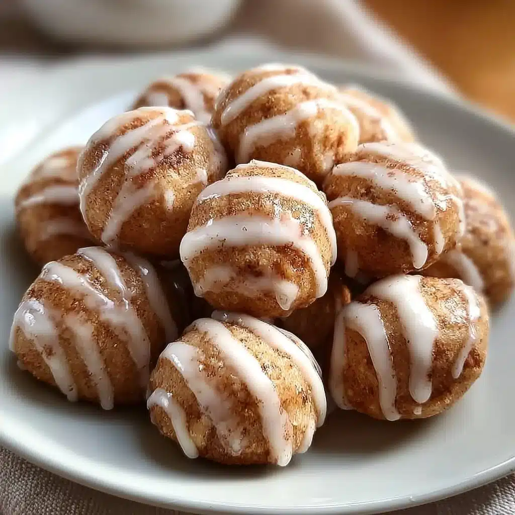 Cinnamon roll protein bites in a bowl with cinnamon sticks and a drizzle of icing.
