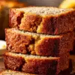 Sliced classic banana bread on a wooden board with ripe bananas